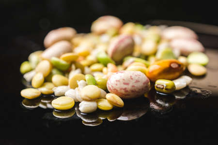 Close up shot of different kind of legumes on a black reflective surfaceの写真素材