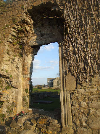 View of new church in county Clare, Ireland through the window of old nearby church ruinsの写真素材