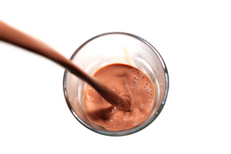 Chocolate milk being poured into a glass on white backgroundの写真素材