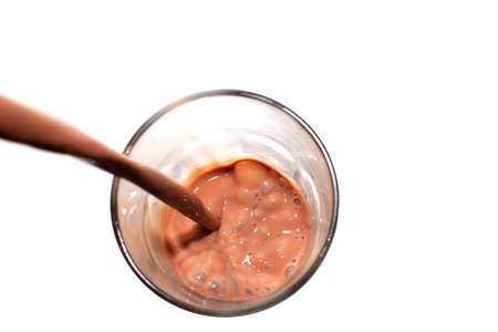 Chocolate milk being poured into a glass on white backgroundの写真素材