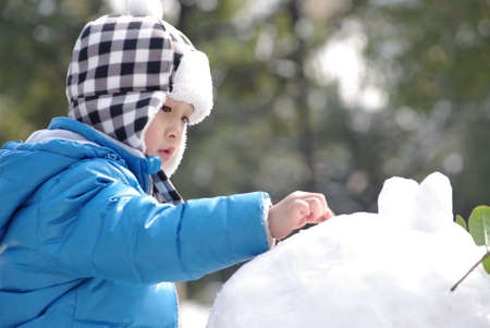 a cute boy is playing snow in winterの写真素材