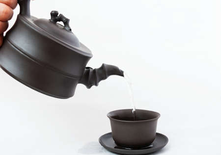 pouring tea from teapot to a cup on a white backgroundの写真素材