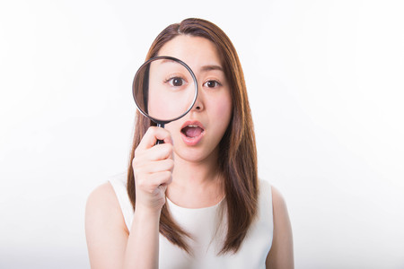 Young woman looking through a magnifying glass on a white backgroundの写真素材