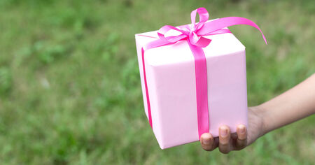 Young boy hand hold pink gift box against nature backgroundの写真素材