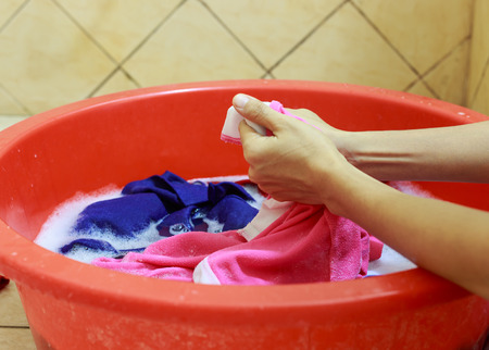 Two hands washing clothes in red tubの写真素材