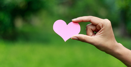Hands holding pink heart paper against nature backgroundの写真素材