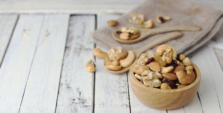 Bowl of mixed nuts with dried berry and wooden spoon with nuts on wooden tableの写真素材