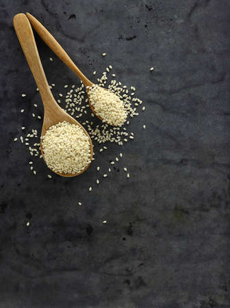 Top view of white sesame seeds on wooden spoon against black background - Flat layの写真素材