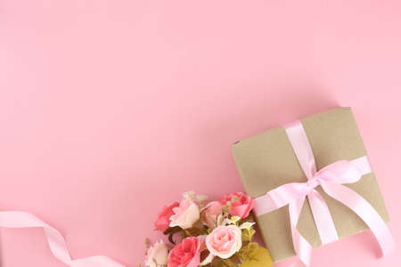 Top view brown paper gift box with pink satin curly ribbon bow and flower on pastel pink background. Flat lay mother day, father day, valentines day, birthday concepts with copy space.の写真素材
