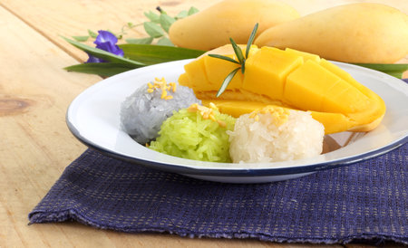 Thai famous delicious dessert - Closeup plate of sweet fresh ripe mango with three color of sticky rice , green from pandan and purple from butterfly pea flower.の写真素材