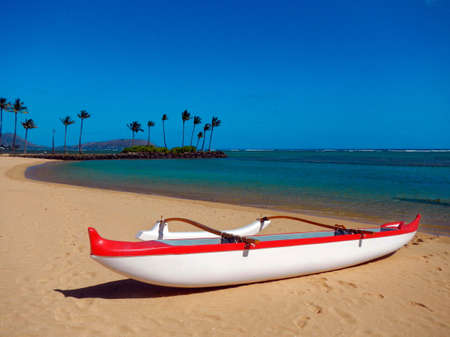 Red and white outrigger canoe was sandy beach and blue sky in Hawaiiの写真素材