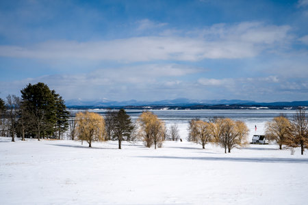 Beautiful winter landscape with lake and snow covered trees in the foregroundの写真素材