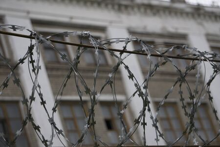 Barbed wire barrier with beautiful sky clouds and brick building behind the scene.