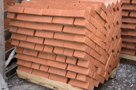 Red clay building bricks stacked on pallets still wrapped in their plastic for delivery at a...