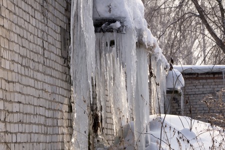 Many icicles hanging on the roof. Large and heavy icicles hanging from the roof of the building. Transparent icicles made from frozen snow meltingの写真素材