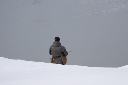 The active man is fishing on sea from the rocky coast. Fisherman check pushing bait on the fishing line, prepare rod and than throw lure into cold water. Fisherman silhouette at sunsetの写真素材