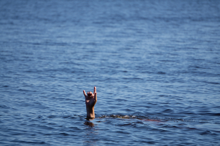 pair of masculine hands sticks out of the sea water on a summer day, a gesture of a man who sinks, copy spaceの写真素材