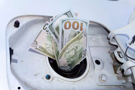 Money sticking out of automobile fuel tank opening signifying and illustrating the high cost of gasの写真素材