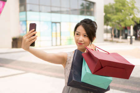 asian girl with shopping bags taking selfieの写真素材