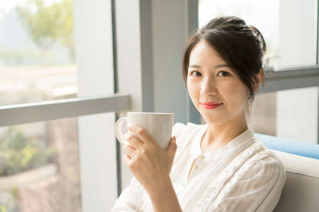 Woman sitting on the sofa holding a coffee cupの写真素材