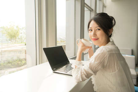 office lady sitting in front of a laptop next to a windowの写真素材