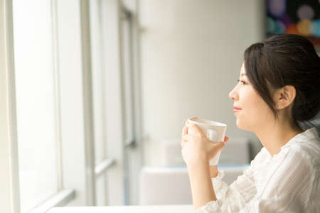 office lady holding a glass cup next to a windowの写真素材