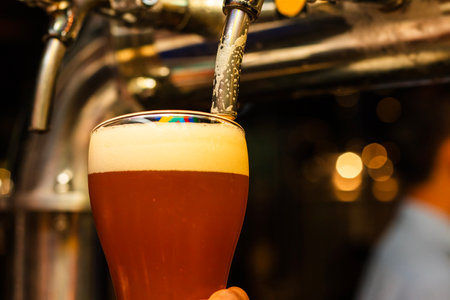 Beer is poured into a glass on the background of the bar counterの写真素材