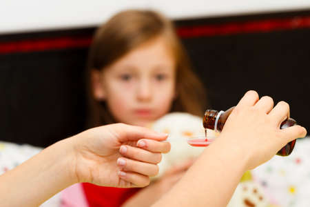 Mother pouring tasty syrup to ease her little girl's cough.の写真素材