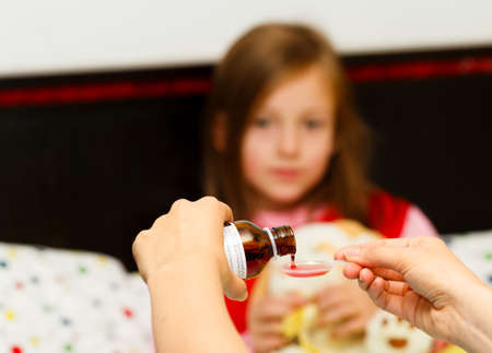 Mother pouring tasty syrup to ease her little girl's cough.の写真素材
