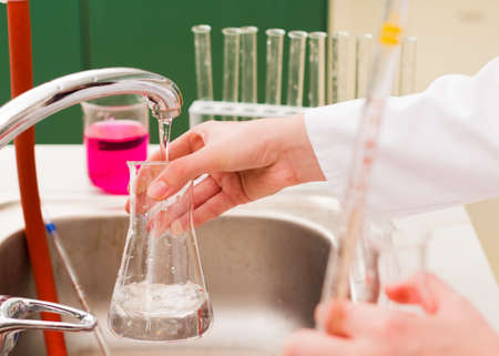 Young woman watering flask to clean it at laboratory.
