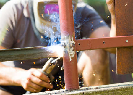 Metal fence assembly by manual worker with protective helmet.