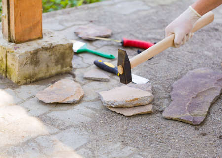 Hand with protective glove splitting stone with hammer to fix it on the tube to design it.の写真素材