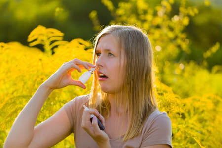 Blond woman breathing with her mouth and applying nose drops because of pollen allergy.の写真素材