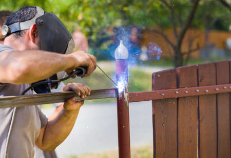 Diy workman welding metal part of gate with flames.