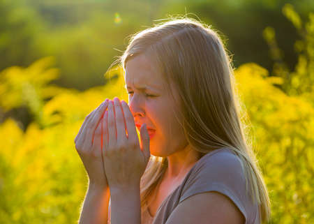 Attractive young woman sneezing because of asthmatic allergy in summer nature.の写真素材