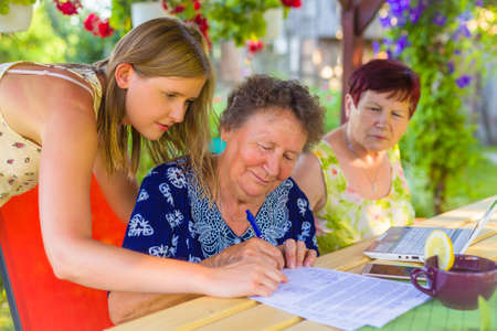 Pensioner signing  legacy heritage testament document near a  witness for her granddaughter.
