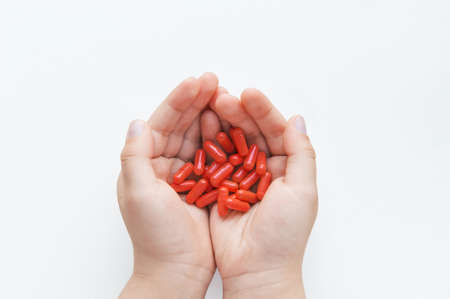 the child holds pills in his hands, orange capsules in children's palms on a white background.