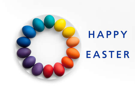 Easter eggs of rainbow colors are arranged in a circle on a white plate and white background