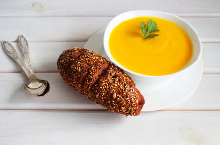 Pumpkin soup on a wooden table with a spoon and bread
