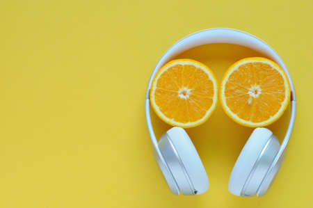 Slice orange fruit and over-ear headphone isolated on yellow color background for summer time with...