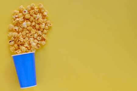 Sweet Caramel Popcorn in blue paper bucket isolated on yellow background with space for text.