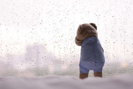 A lonely Teddy Bear crying at window with rain drop on the glass in rainy day with space for text.