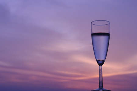 The glass of sparkling wine isolated on background of dusk sky and sunset with space for text.