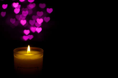 White aromatic glass candle with flame and pink love shape bokeh on dark background for Christmas holiday.の写真素材