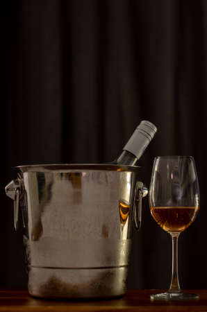 A glasses of Rose wine on wooden table with a bottle in wine chiller bucket to celebrate with dark...