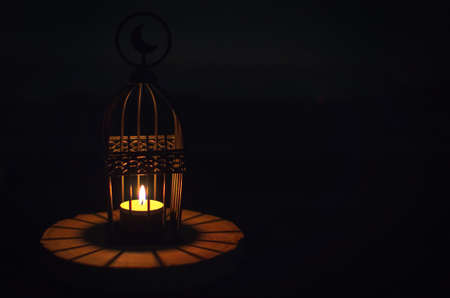 Beautiful Lantern that have moon symbol on top that have light from candle shining on wooden tray with dark background for the Muslim feast of the holy month of Ramadan Kareem.の写真素材