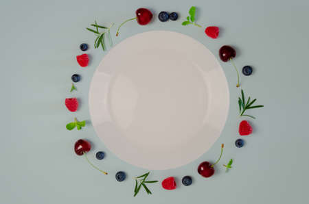 Fresh cherry, blueberry, raspberry, mint and rosemary leaf on top view with white plate and pastel blue color background for healthy food concept.の写真素材