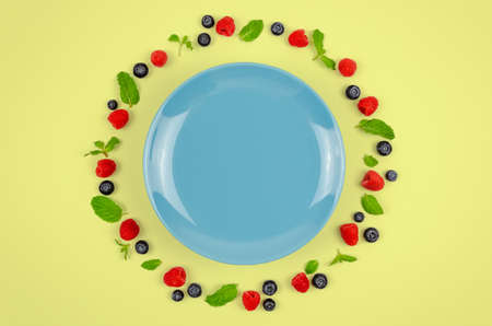 Fresh blueberries, raspberries and mint leaf on top view with blue plate and pastel yellow color background for healthy food concept.の写真素材
