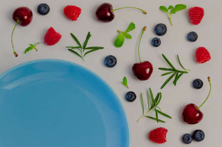 Fresh cherries, blueberries, raspberries, mint and rosemary leaf on top view with blue plate and pastel gray color background for healthy food concept.の写真素材