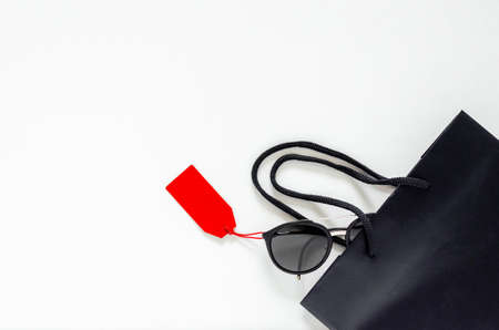 Flat lay of black sunglasses with red price tags and shopping bag on white background for Black...